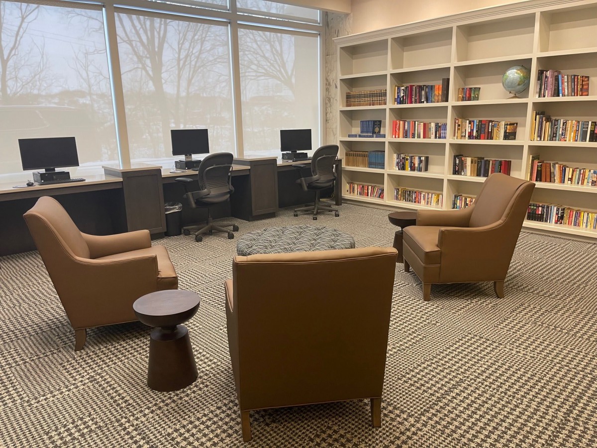 A cozy library reading area featuring comfortable chairs, bookshelves, and computer stations.