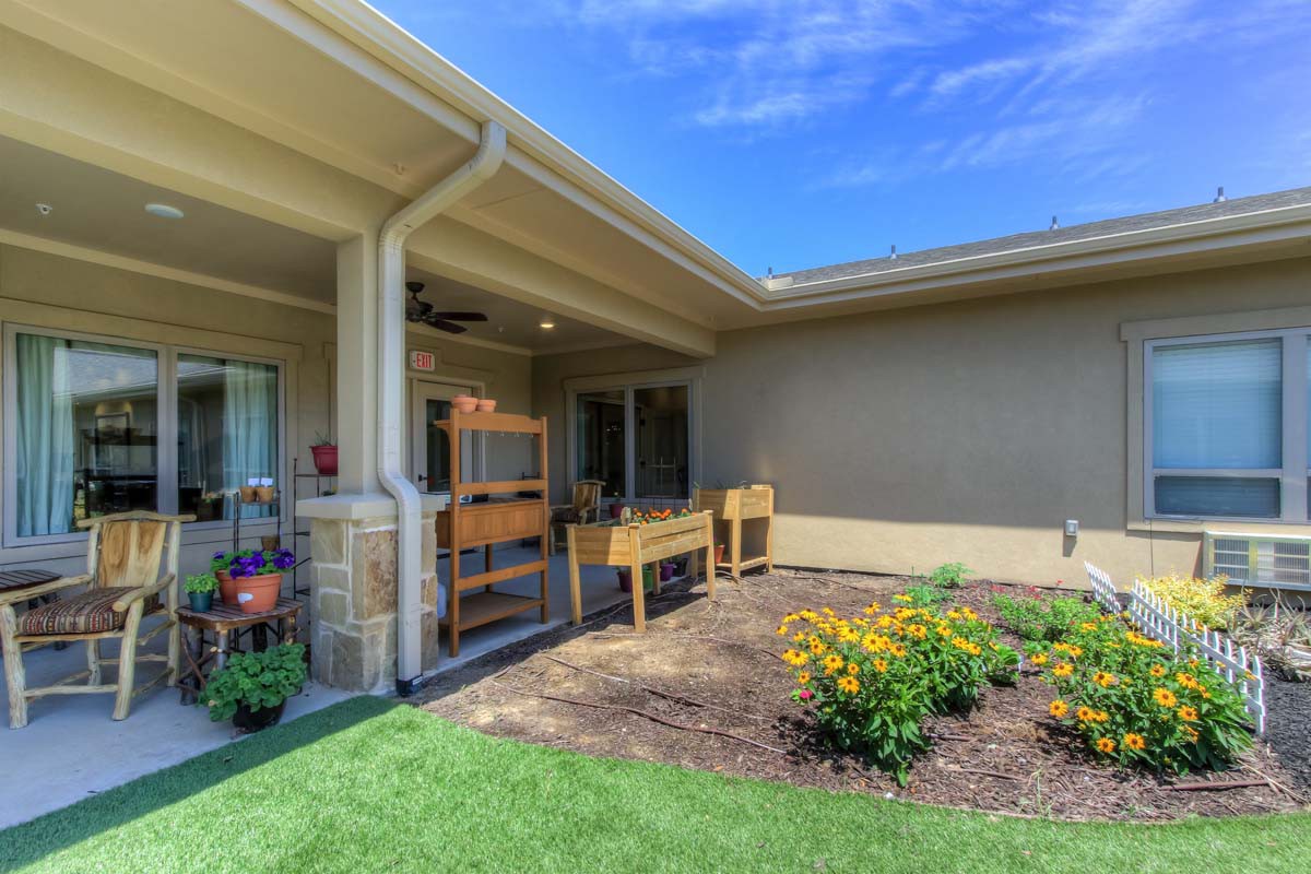 A sunny backyard patio with raised planters and a garden area featuring vibrant flowers.