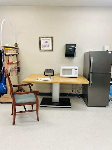 A cozy break area featuring a chair, table, microwave, and refrigerator.