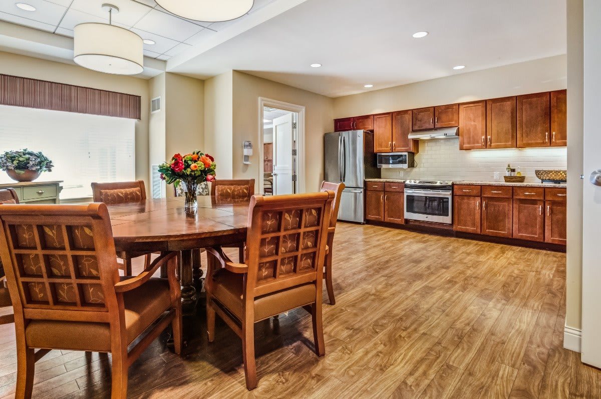 A modern kitchen and dining area with wooden floors, featuring a large dining table, chairs, and stainless steel appliances.