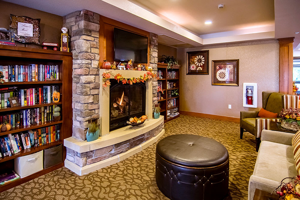 A cozy living room with a stone fireplace, adorned with autumn decorations and surrounded by bookshelves.