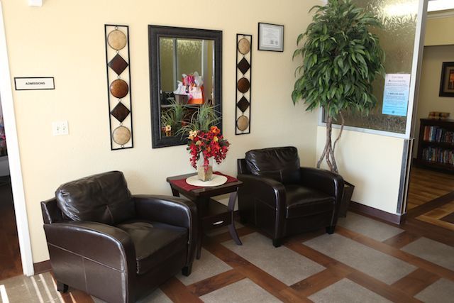 A cozy waiting room with two leather chairs, a small table with flowers, a mirror, and decorative wall art.