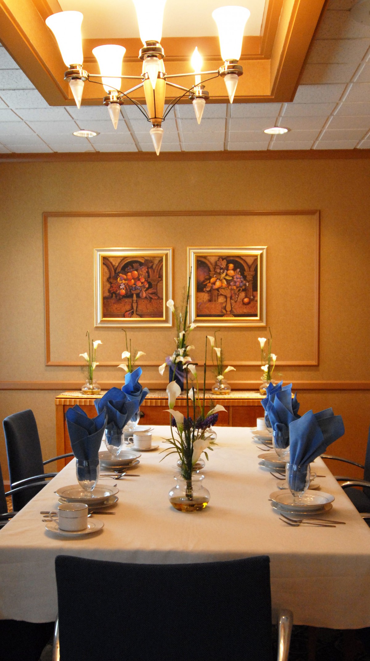 An elegantly set dining table with blue napkins, candles, and framed artwork on the wall.