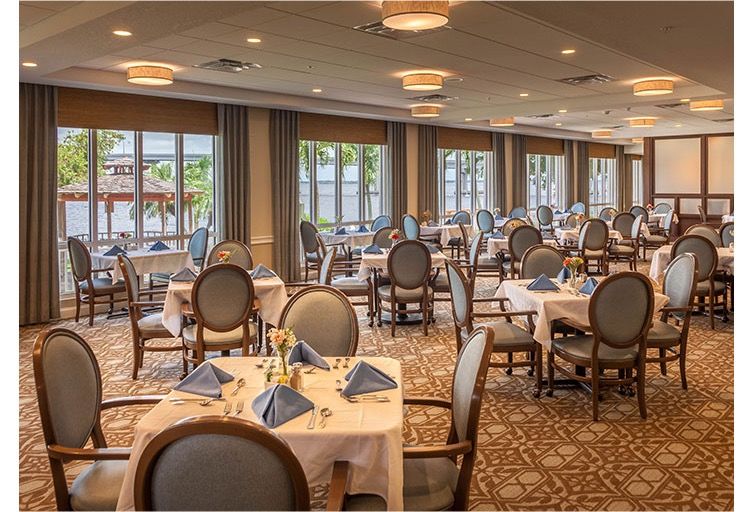 An elegant dining room with neatly arranged tables and chairs, set with blue napkins.