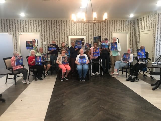 A group of people proudly displaying their paintings in an art class setting.
