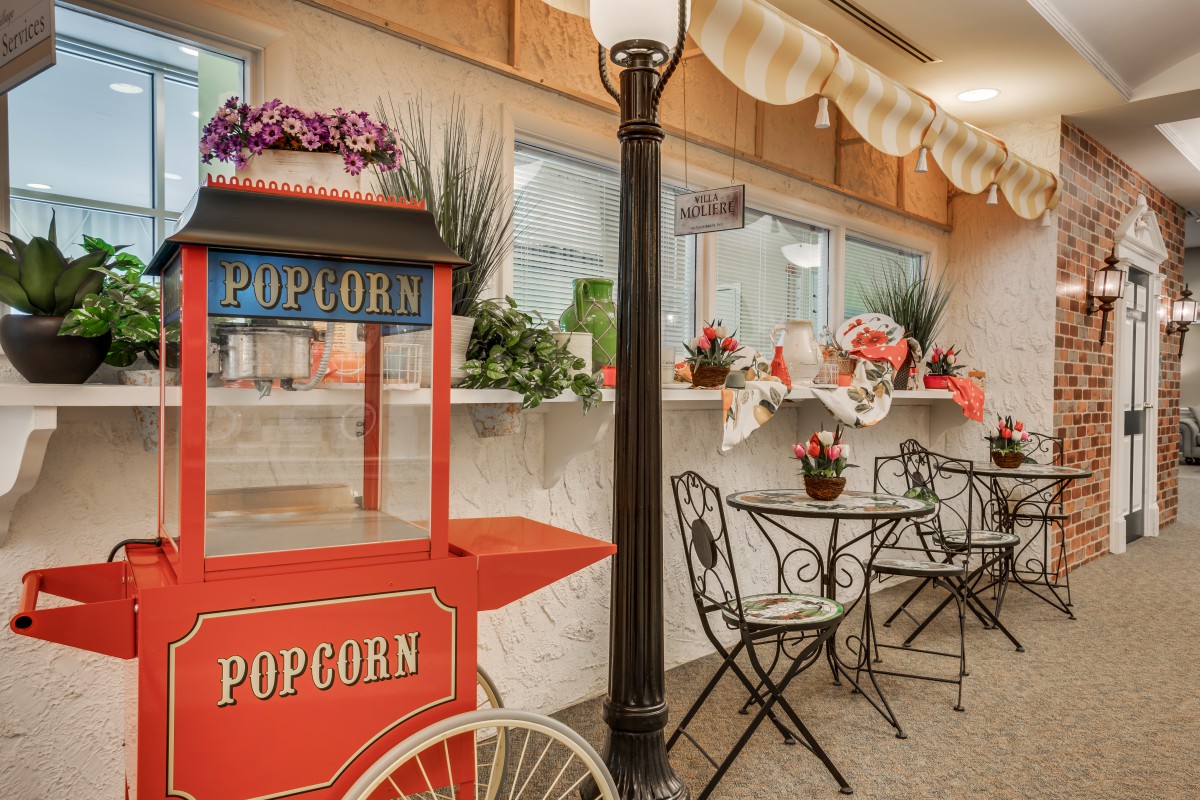 A charming indoor cafe setting with a vintage popcorn cart and decorative flowers.
