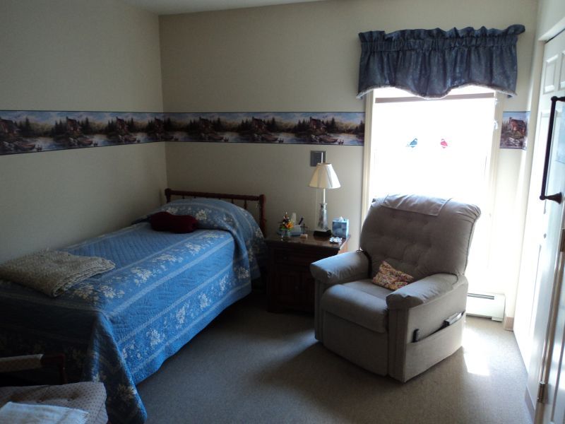A cozy bedroom with a bed, reclining chair, and a window letting in natural light.