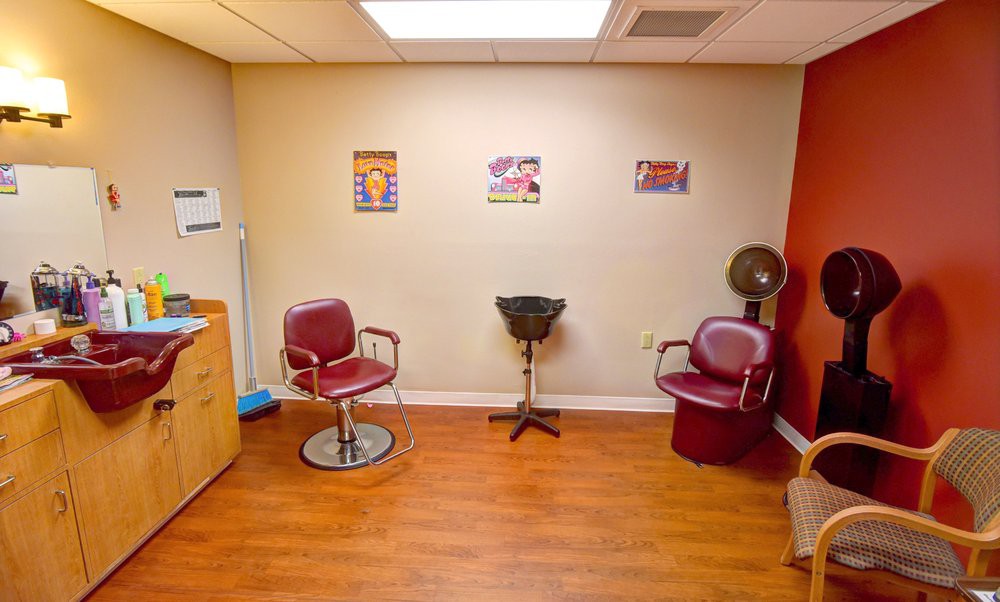An interior view of a hair salon featuring chairs, a hair dryer, and a wooden floor.