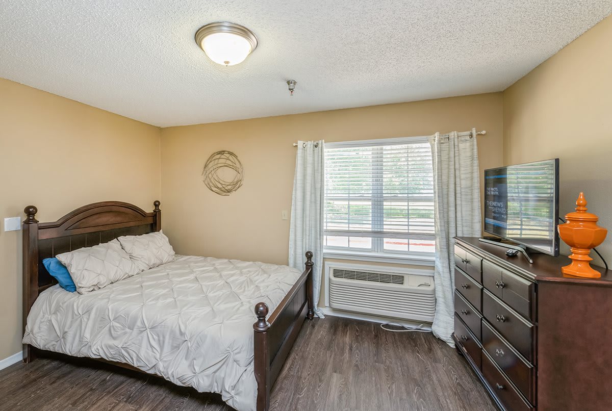 A cozy bedroom featuring a wooden bed, dresser, and a window with curtains.