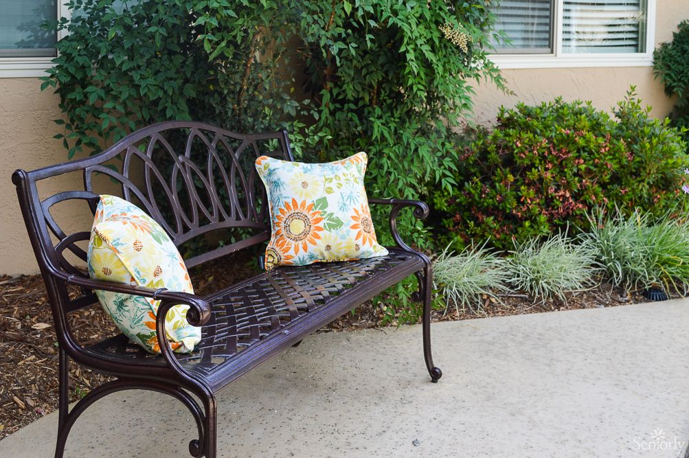An outdoor bench with decorative pillows in a garden setting.