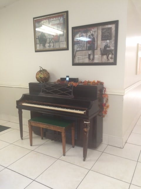 An upright piano with a bench is adorned with autumn decorations, accompanied by framed photos on the wall.