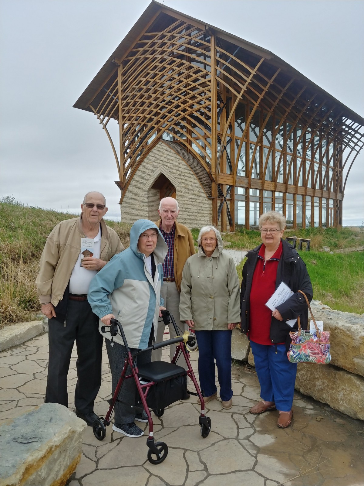 A group of elderly people posing in front of an outdoor architectural structure.