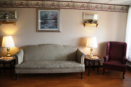 A cozy living room setup featuring a beige sofa, a purple armchair, a table lamp, and decorative artwork on the wall.