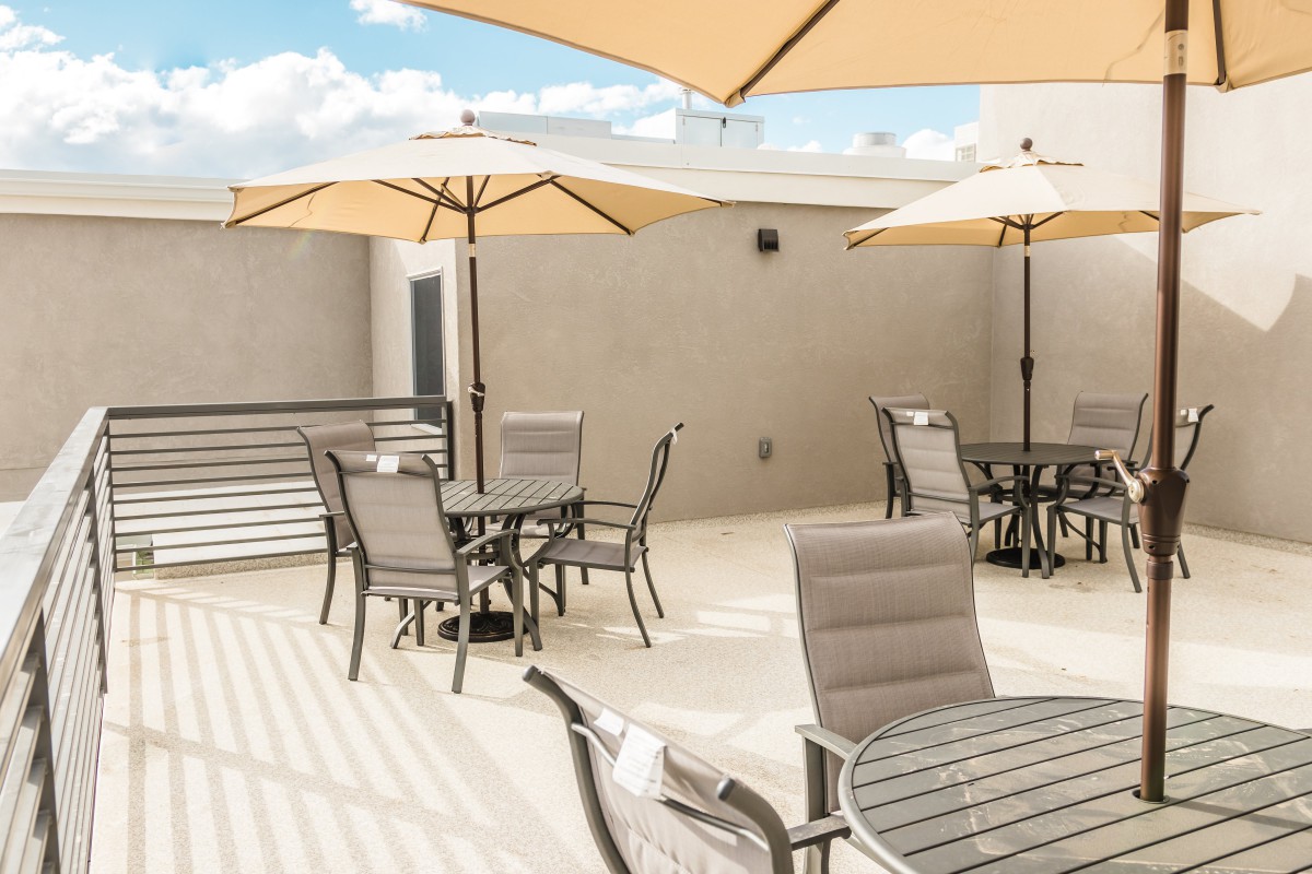 A sunny outdoor patio with tables, chairs, and umbrellas.