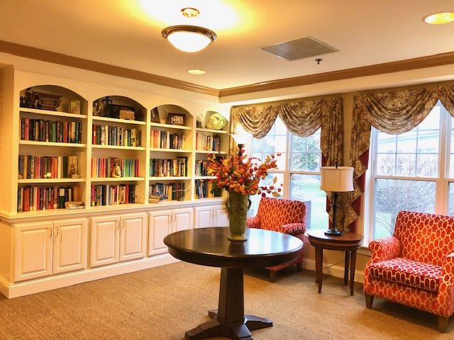 A cozy library room with a central table, bookshelves, and comfortable seating.