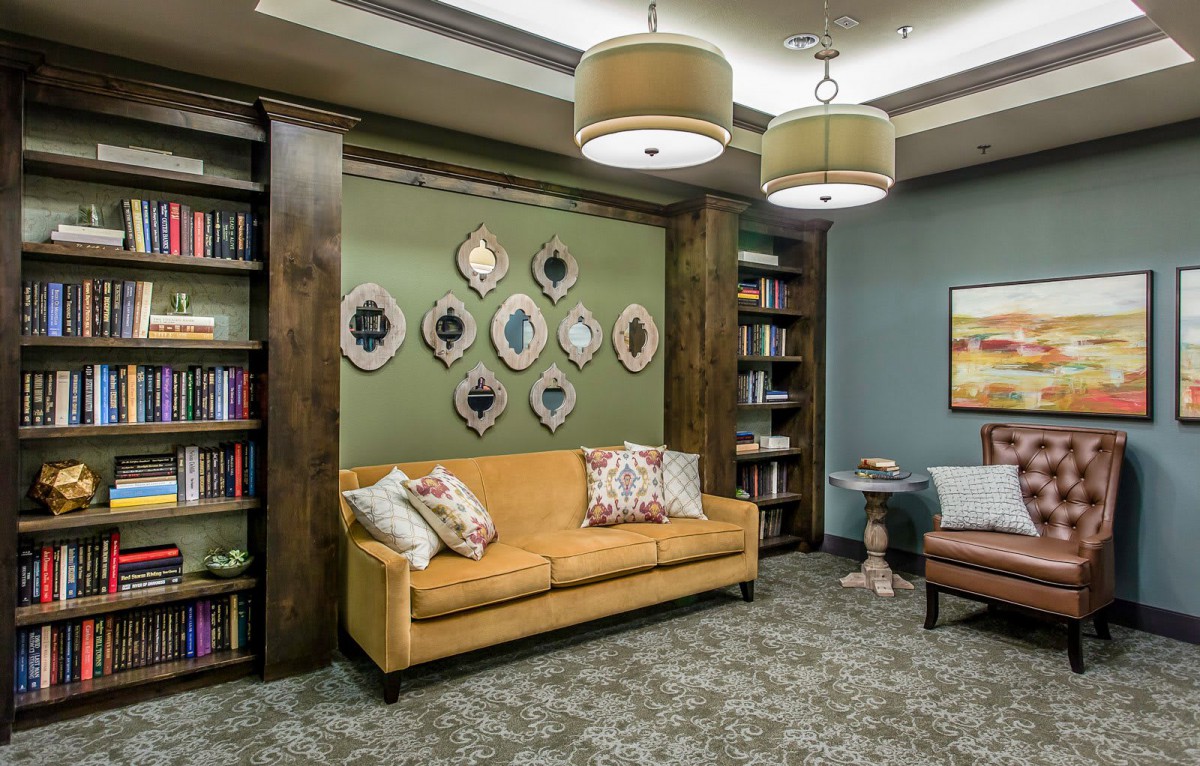 A cozy living room with a mustard couch, decorative frames on the wall, and bookshelves.