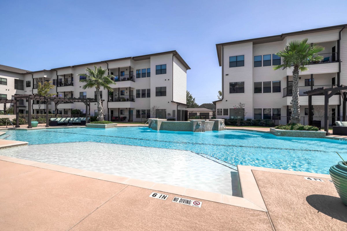 A modern apartment complex featuring a refreshing outdoor swimming pool under a clear blue sky.