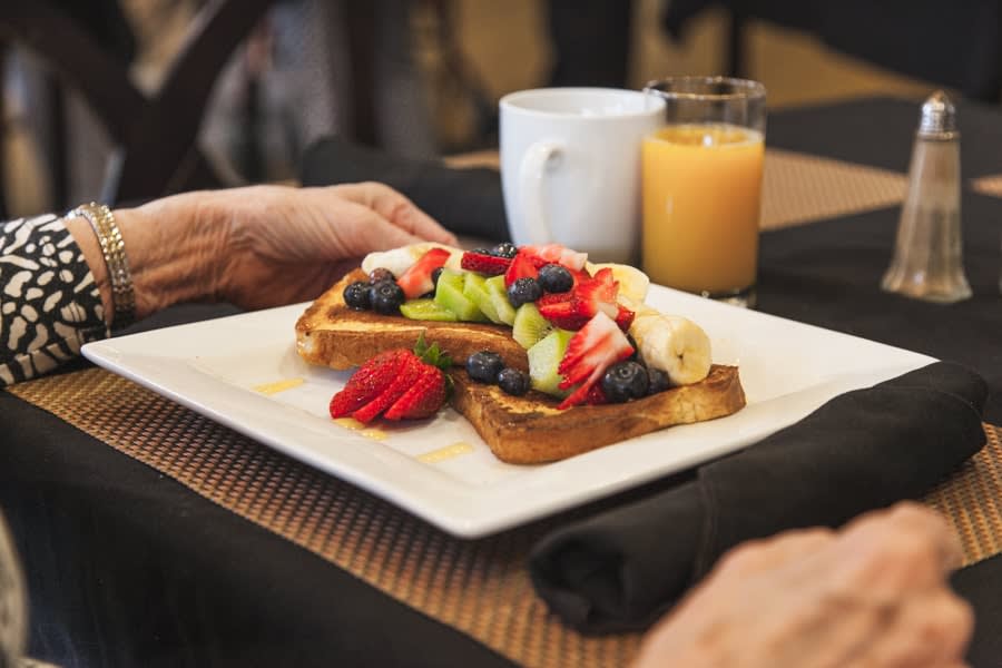 A breakfast plate featuring toast topped with fresh fruit and berries, accompanied by orange juice and coffee.
