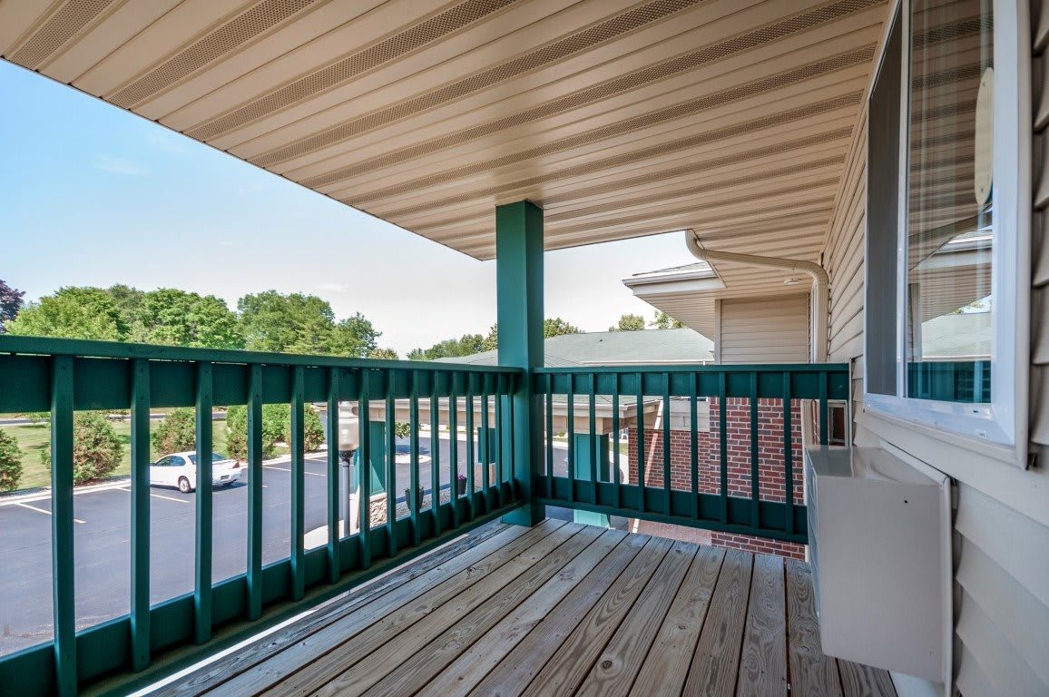 A covered balcony with a wooden floor and railing, offering a view of the surrounding area.