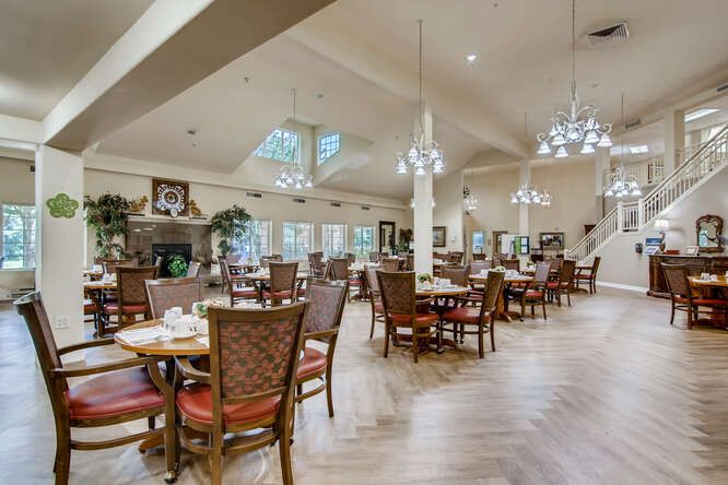 A spacious and elegant dining room with multiple tables and chairs, illuminated by chandeliers.