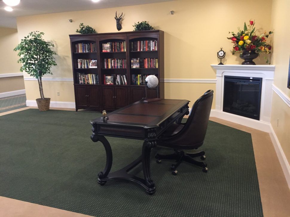 A cozy office space featuring a wooden desk, comfortable chair, and a bookshelf filled with books. A fireplace adds to the ambiance of the room.