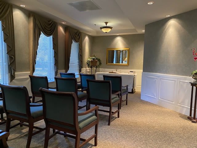 An elegantly decorated room with rows of chairs facing a table and mirror, illuminated by soft lighting.