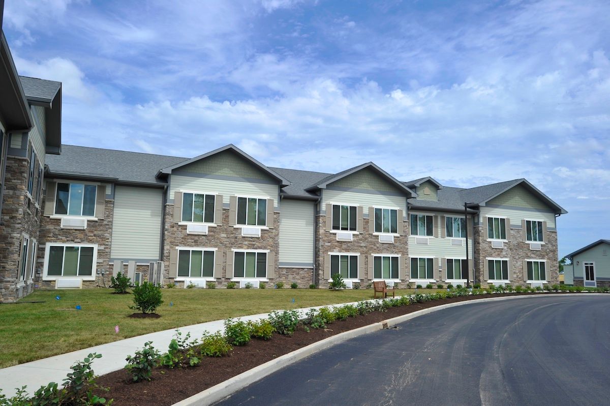 A modern residential building with a landscaped driveway under a blue sky.