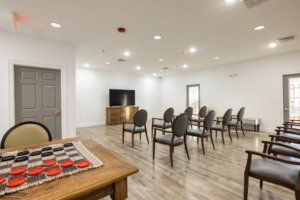 A well-lit meeting room with arranged chairs and a television, featuring a checkers game on the table.