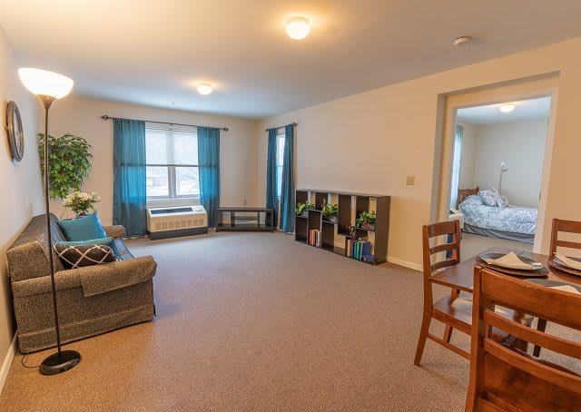 A spacious living room with a sofa, dining area, and large windows adorned with blue curtains.