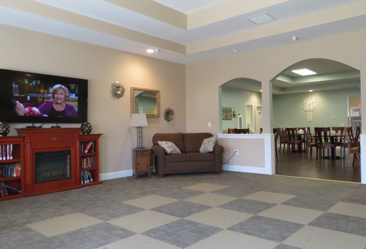 A cozy living room with a sofa, fireplace, and television, featuring artwork and arched doorways.
