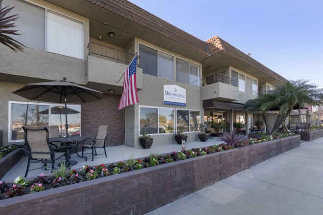 A building with an American flag, patio furniture, and landscaped flowers outside.