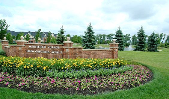 A scenic view featuring a brick sign surrounded by vibrant flowers and lush greenery in a park setting.