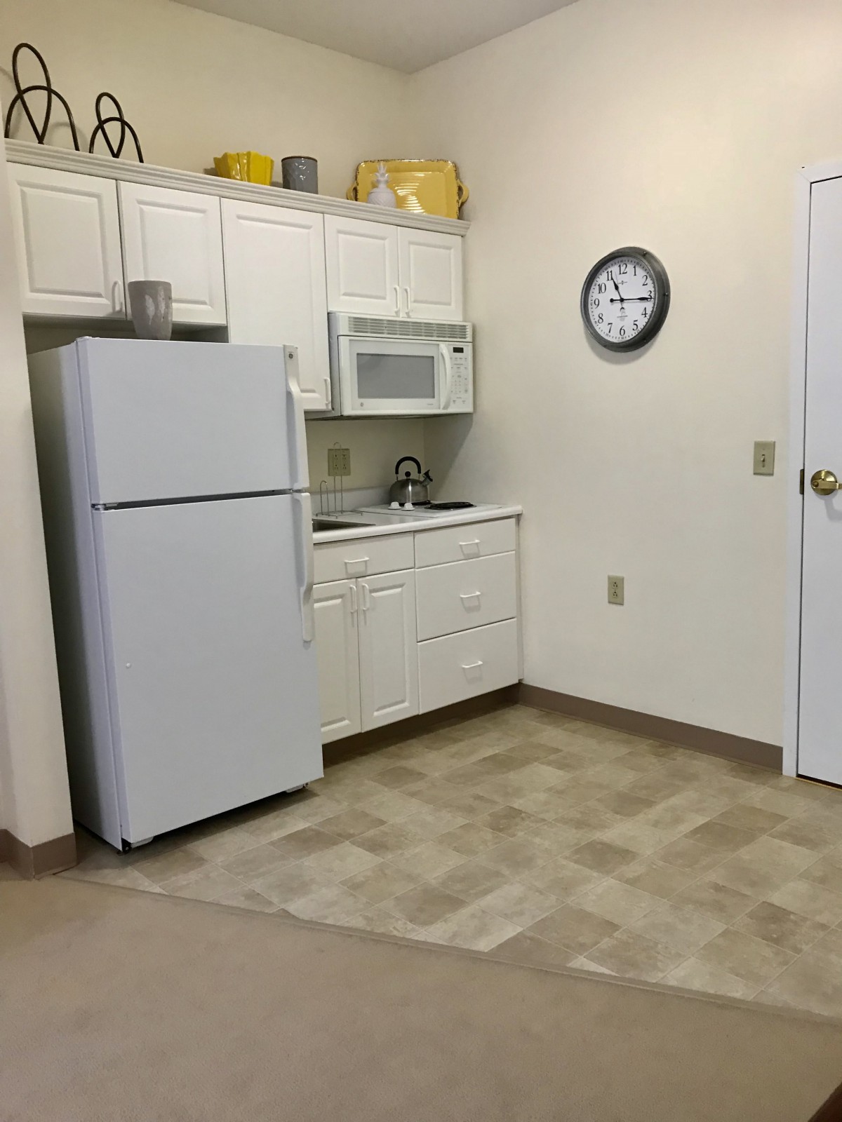 A small kitchen with a refrigerator, microwave, sink, and clock on the wall.