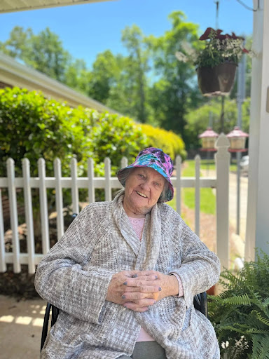 A joyful elderly woman enjoying a sunny day outdoors, dressed comfortably and wearing a colorful hat.