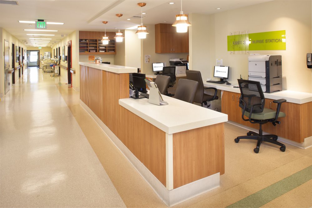 A modern hospital reception area with desks, computers, and office chairs in a well-lit hallway.