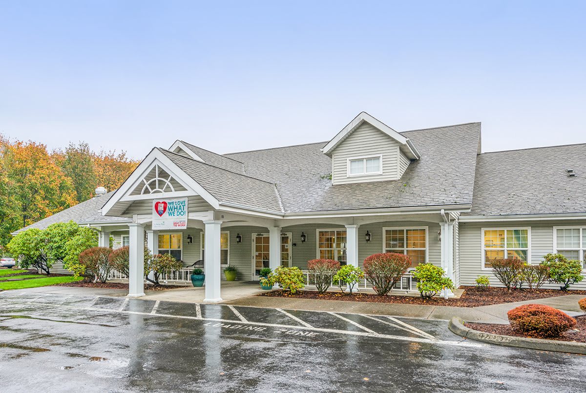 A charming building with a covered entrance and surrounding greenery, seen from the parking lot on a rainy day.