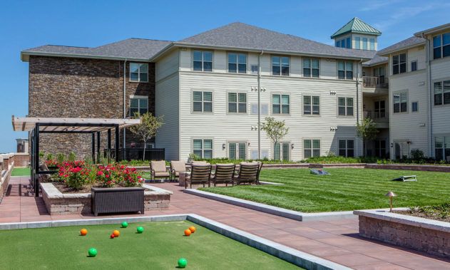 A sunny outdoor area featuring a bocce court, patio furniture, and a large building.