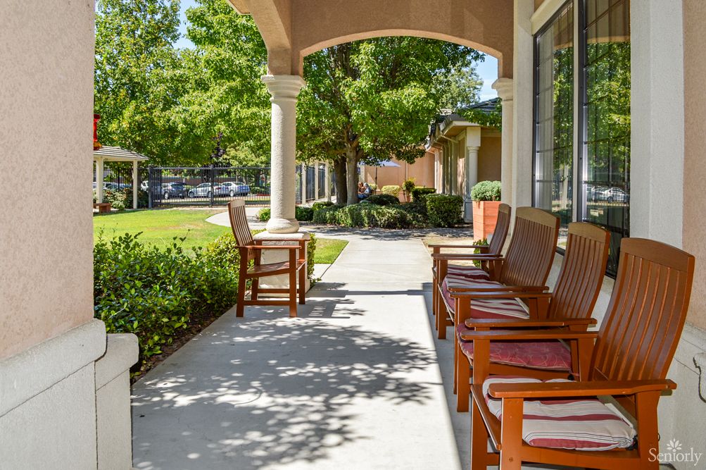 A peaceful veranda with wooden chairs under the shade, overlooking a garden with trees.