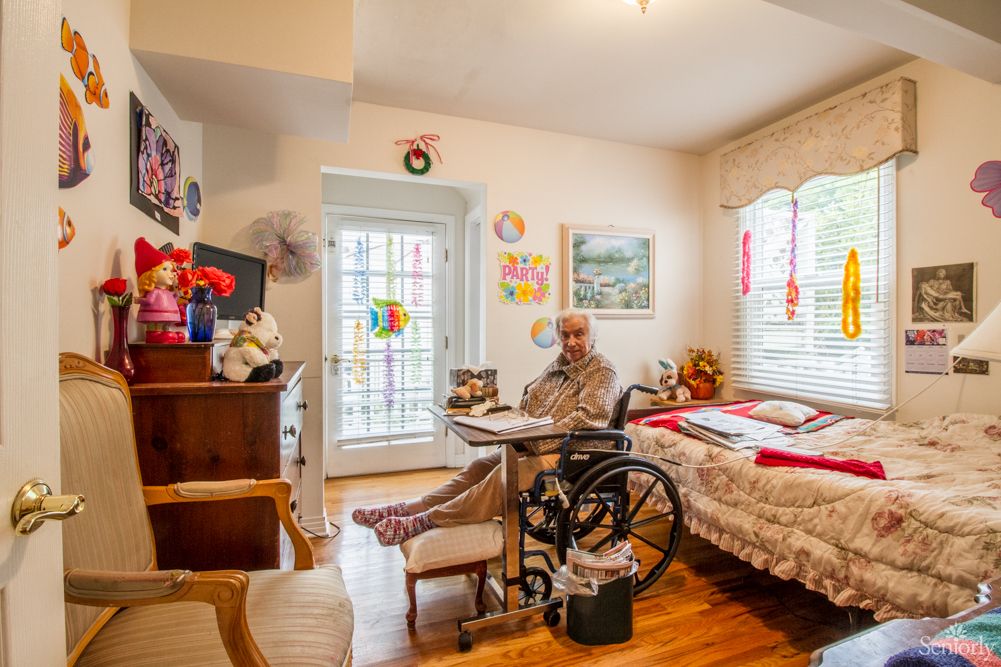 An elderly person sitting in a wheelchair in a warmly decorated bedroom.