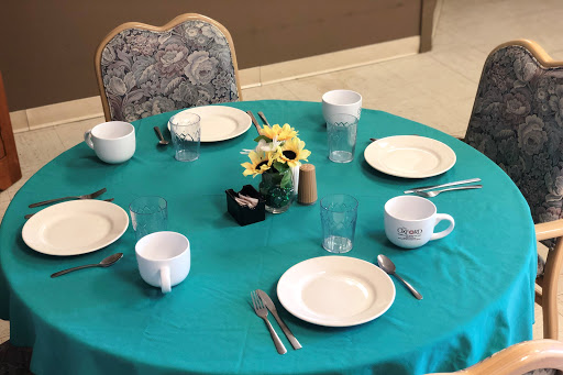 A neatly arranged dining table featuring a turquoise tablecloth, plates, cups, and a floral centerpiece.