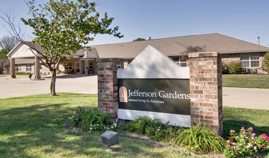 Entrance sign for Jefferson Gardens with a background view of the building and greenery.