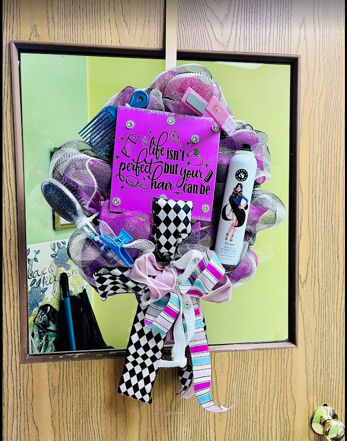 A colorful wreath with ribbons and a humorous sign hangs on a door mirror.