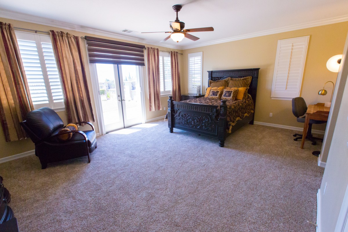A spacious bedroom with a large bed, elegant curtains, and a ceiling fan.