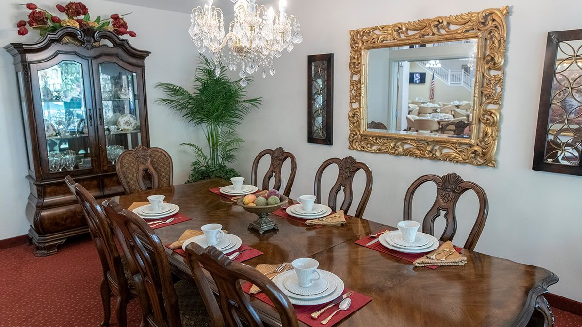 An elegantly set dining room featuring a chandelier, wooden dining table, and mirror.