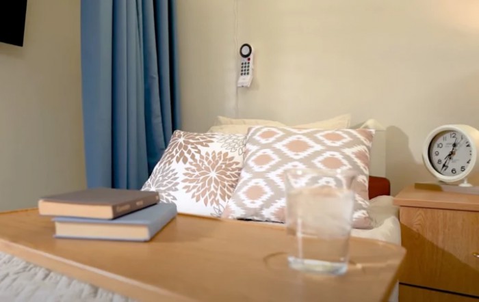 A cozy bedroom setup featuring patterned pillows, a stack of books, and a glass of water on a nightstand.