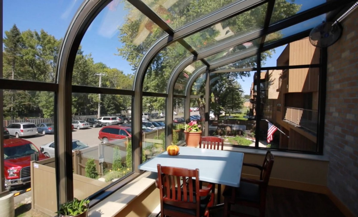 A cozy sunroom with a glass ceiling and walls, featuring a table and chairs overlooking an outdoor view.