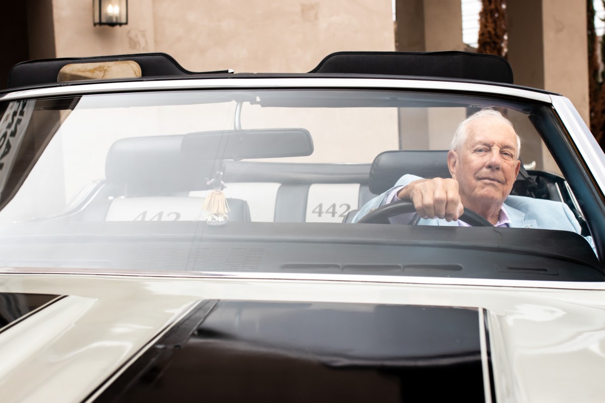 A man driving a convertible car outside a building.