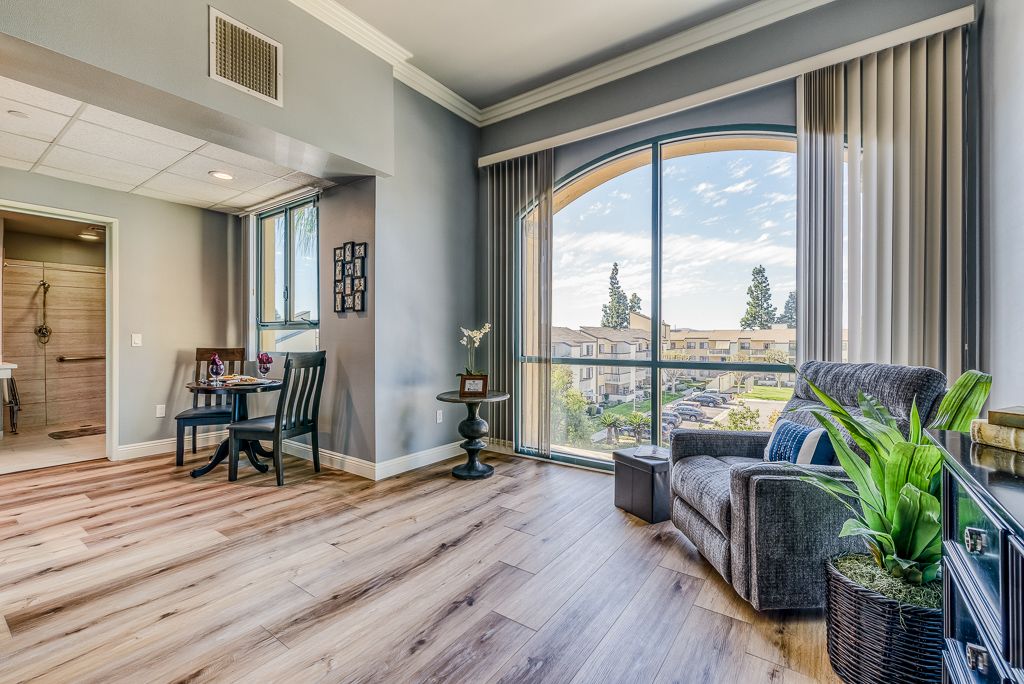 A cozy living room with a large window, featuring an armchair and wooden flooring that enhances the natural light.
