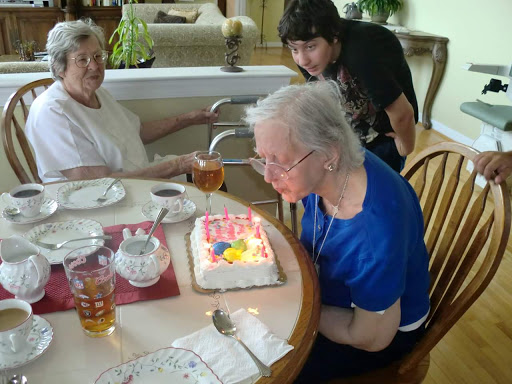 A joyful birthday celebration with family, featuring an elderly woman about to blow out the candles on her cake.