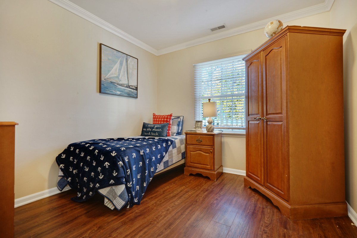 A cozy bedroom with a nautical-themed single bed, wooden wardrobe, and nightstand next to a window.
